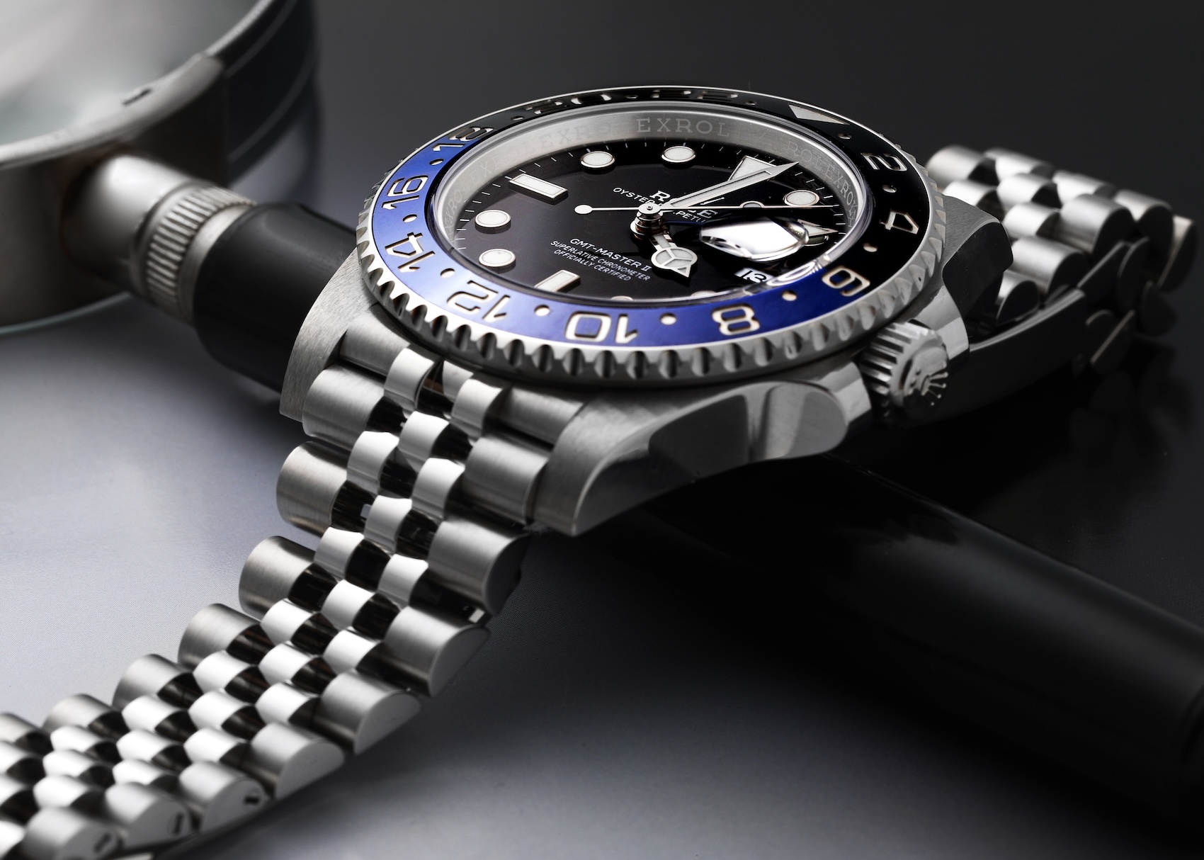 Rolex GMT-Master II Batgirl 126710BLNR lying flat next to a watchmaker's loupe, focusing on the black and blue bezel and Jubilee bracelet.