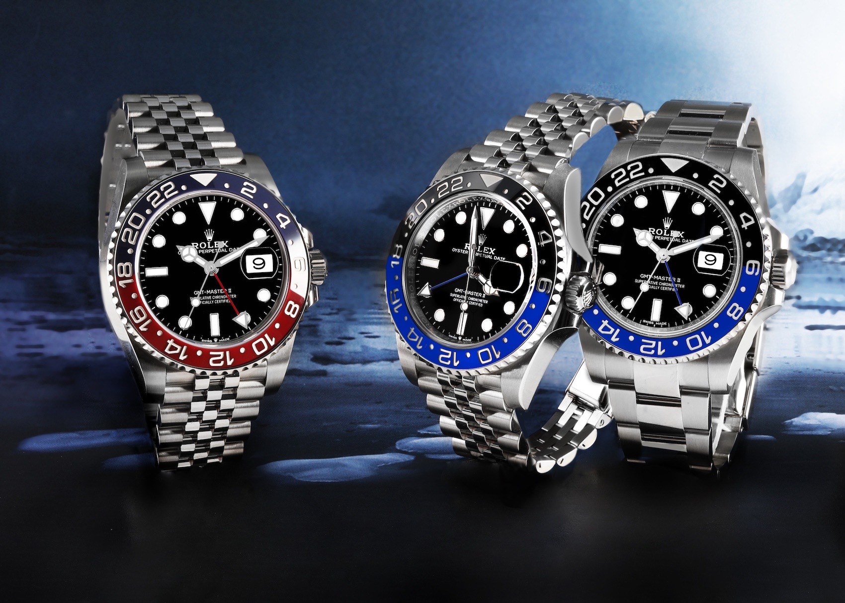 Rolex GMT-Master II Pepsi and Batgirl models placed side-by-side on an icy blue background, showcasing their Cerachrom bezels.