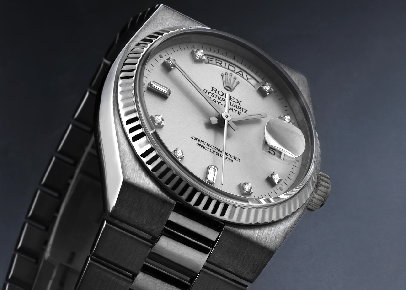 Side perspective of a Rolex Oysterquartz President Day-Date in white gold with fluted bezel, silver dial, diamond markers, and the integrated President bracelet on a blue/dark gradient background.