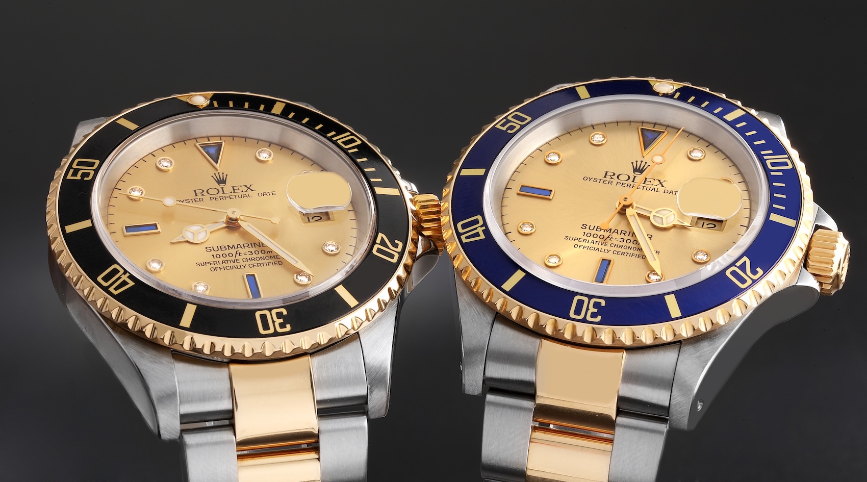 An overhead comparison shot showing two two-tone Rolex Submariner Reference 16613 watches. The watch on the left has a rare gold dial and black bezel insert; the watch on the right has an identical rare gold dial and blue bezel insert.