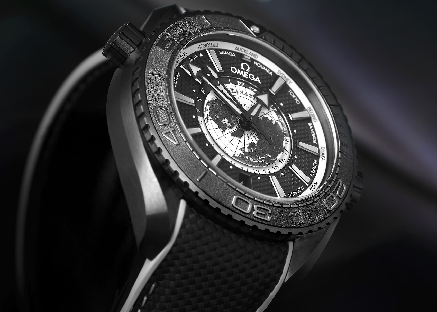 Angled profile view of the Omega Planet Ocean 600M Worldtimer showing its thick brushed black ceramic case and helium escape valve.