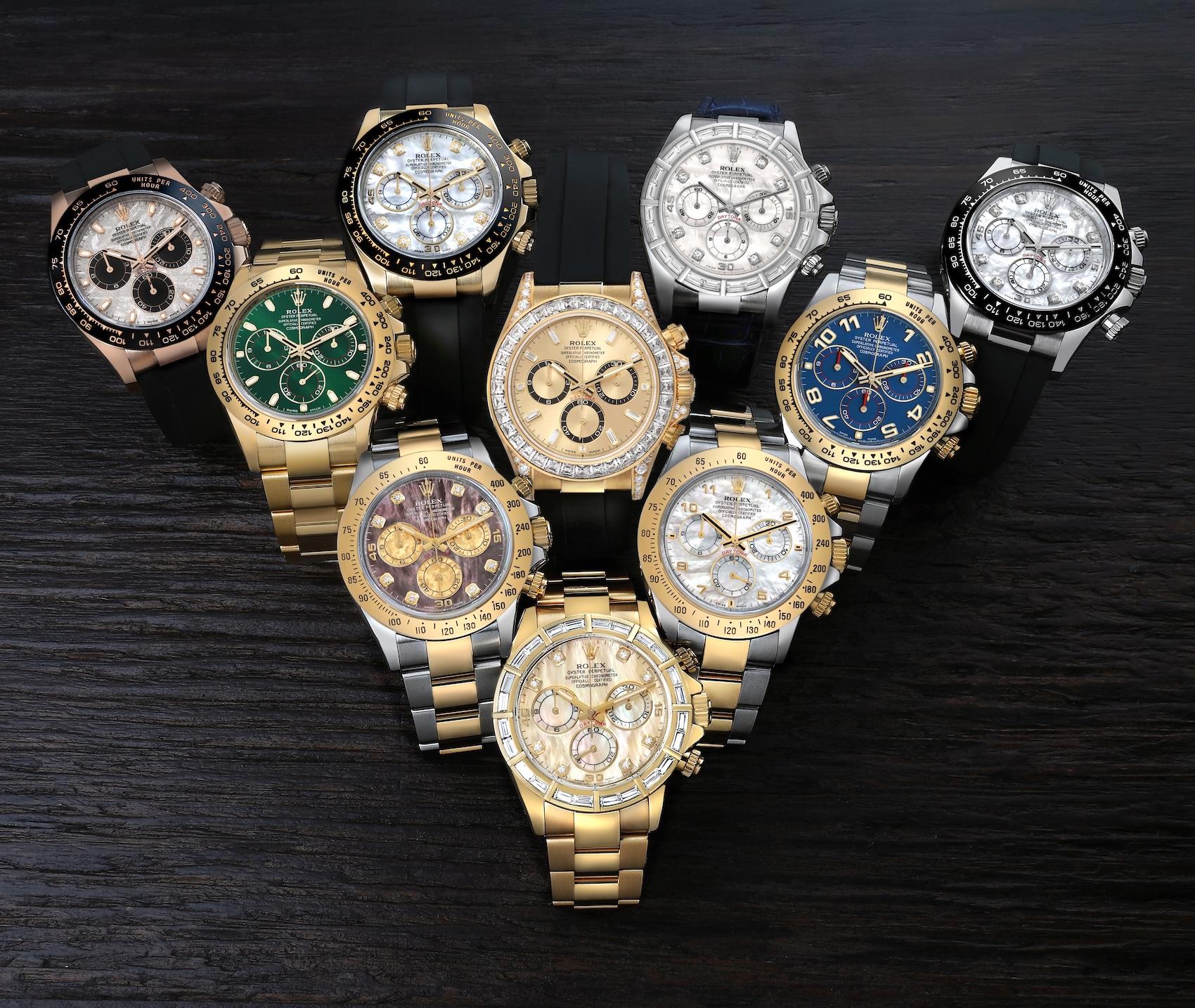 A diverse collection of luxury Rolex Cosmograph Daytona watches in yellow gold, rose gold, and white gold displayed on a dark wooden surface.