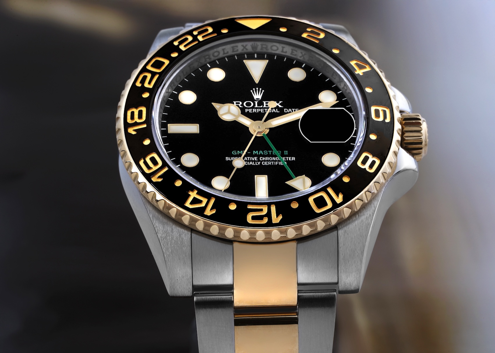 Front view of a two-tone Rolex GMT-Master II 116713LN featuring a black ceramic bezel with gold numerals, a black dial, and a green GMT hand on an Oyster bracelet.