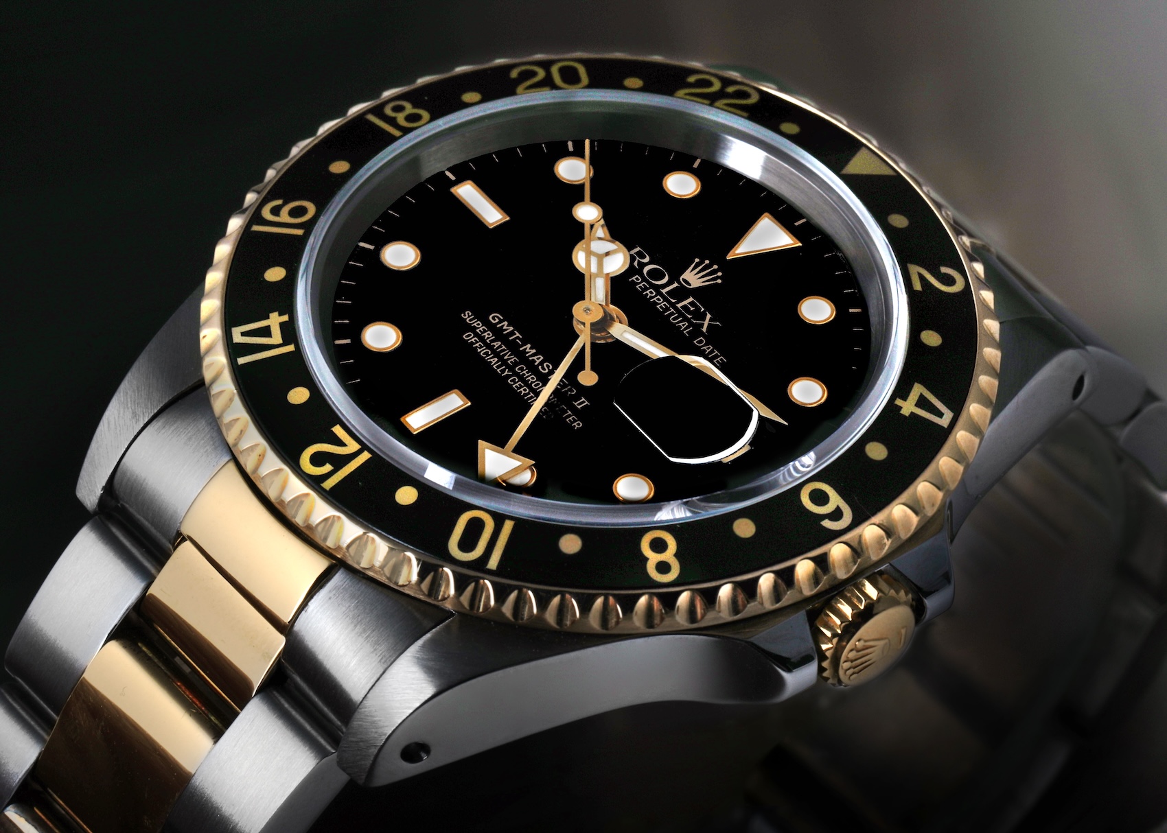Angled close-up of a two-tone Rolex GMT-Master II reference 16713 with a black dial, gold text, gold GMT hand, and a black aluminum bezel insert.