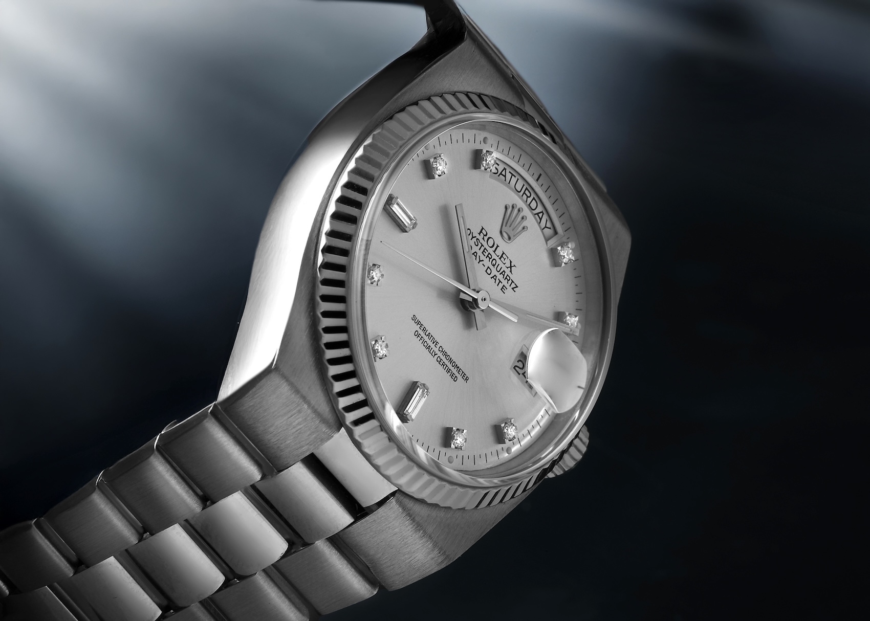 A dynamic, head-on perspective of the white gold Rolex Oysterquartz 19019 watch face, showing dramatic lighting highlighting the silver diamond dial, the fluted bezel, and the 'SATURDAY 2' calendar display.
