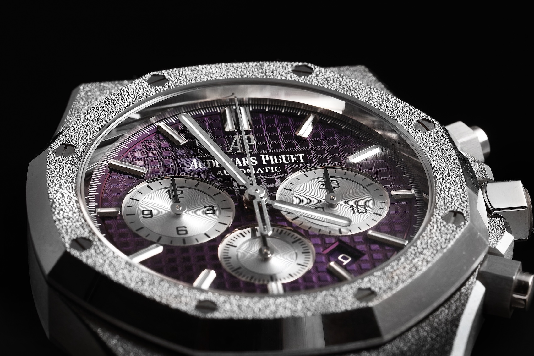 A close-up macro shot of the Audemars Piguet Royal Oak Chronograph Frosted Gold reference 26331BC, highlighting the deep plum dial, silver subdials, and hammered white gold bezel. 