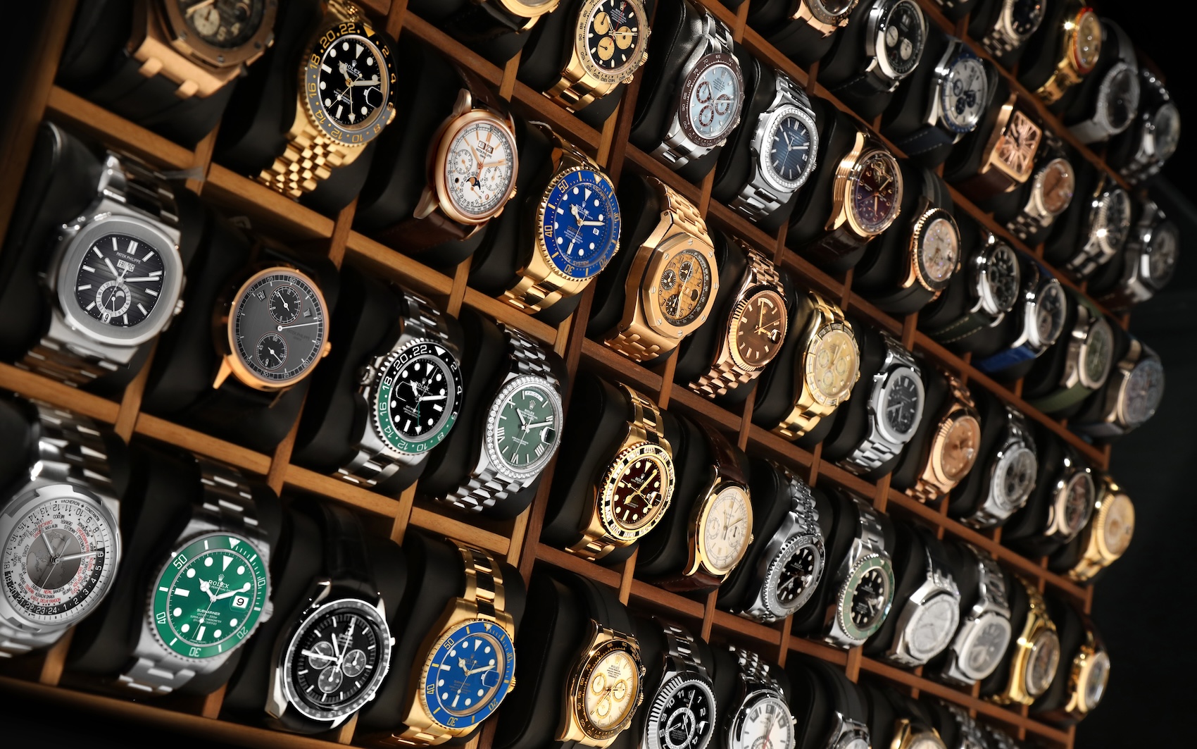 A large collection of luxury watches from brands like Rolex and Patek Philippe organized beautifully inside a wooden display case.