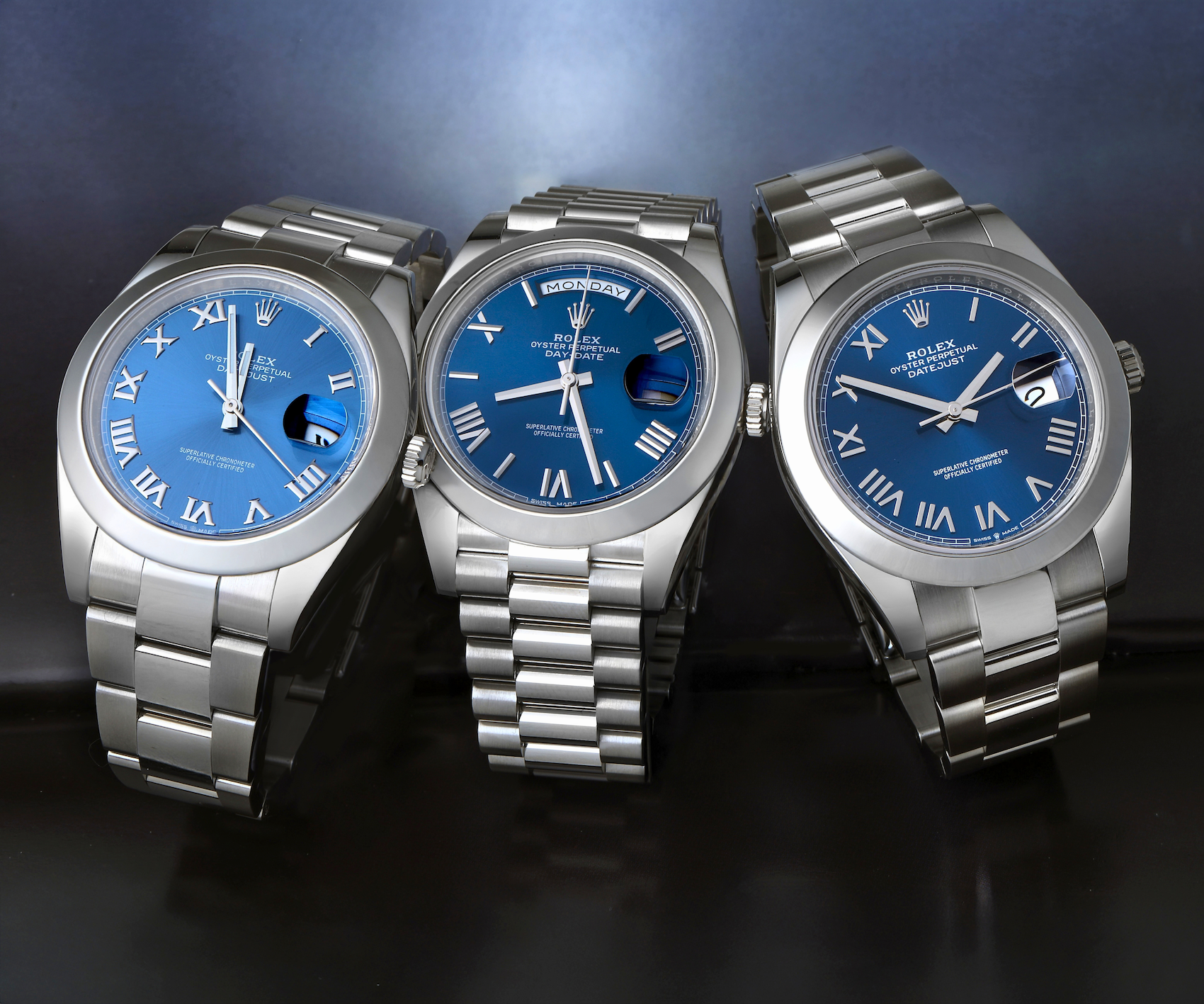 Group of three Rolex watches featuring blue dials with deconstructed Roman numerals, including stainless steel Datejust and Day-Date models.