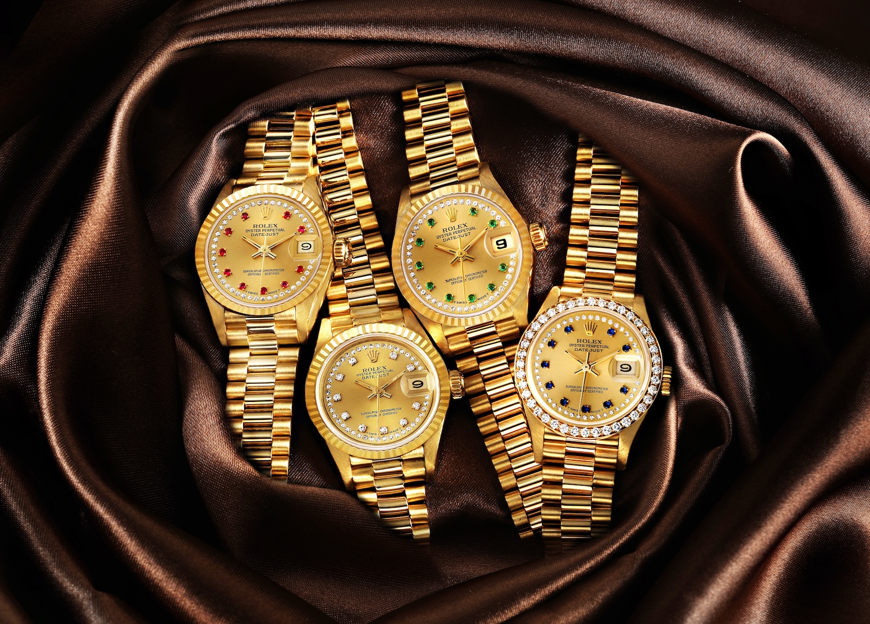 A collection of four 18k yellow gold Rolex Ladies President watches showcasing various factory gem-set dials including rubies, emeralds, sapphires, and diamonds.