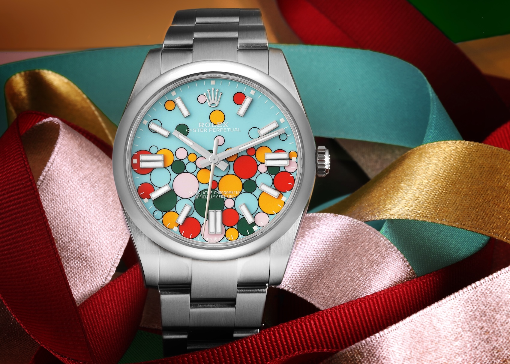 A detailed macro view of the colorful Rolex Oyster Perpetual Celebration dial, featuring 51 asymmetrical, black-outlined bubbles filled with pink, turquoise, yellow, red, and green lacquer, set against a backdrop of celebratory multi-colored metallic ribbons.
