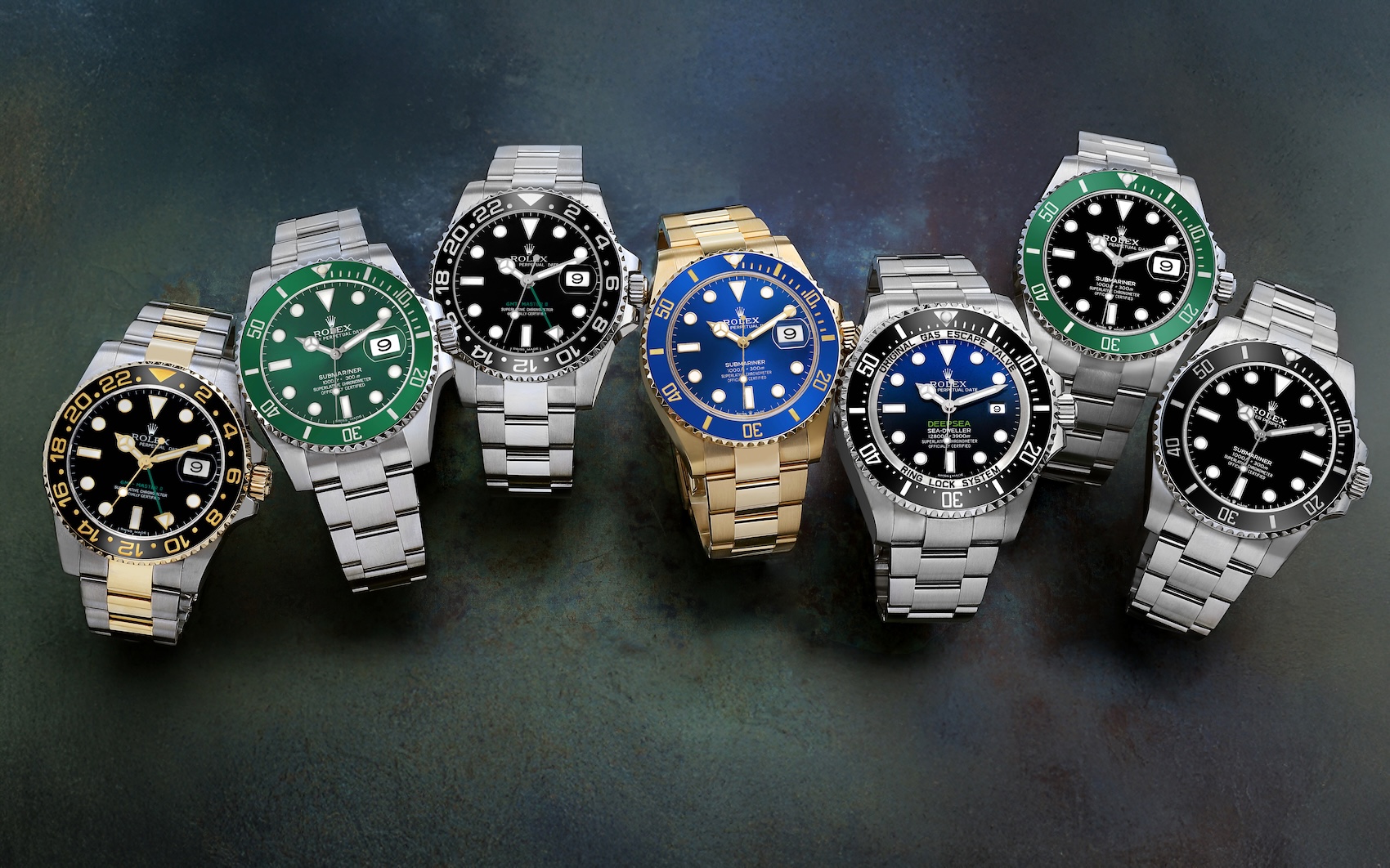 A collection of seven Rolex professional sports watches on a dark surface, featuring various Submariner, GMT-Master II, and Sea-Dweller models in stainless steel, two-tone, and solid yellow gold.