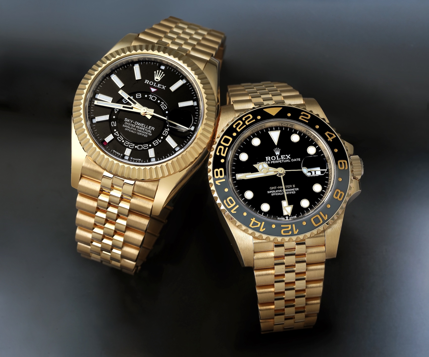 Side-by-side view of a full yellow gold Rolex Sky-Dweller with a black dial and a yellow gold Rolex GMT-Master II with a black and grey bezel.
