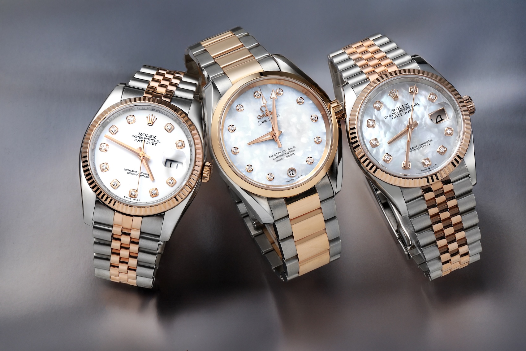 Three stainless steel and 18k rose gold watches featuring a Rolex Datejust with a white diamond dial, an Omega Seamaster Aqua Terra with a mother-of-pearl diamond dial, and a Rolex Datejust with a mother-of-pearl diamond dial.